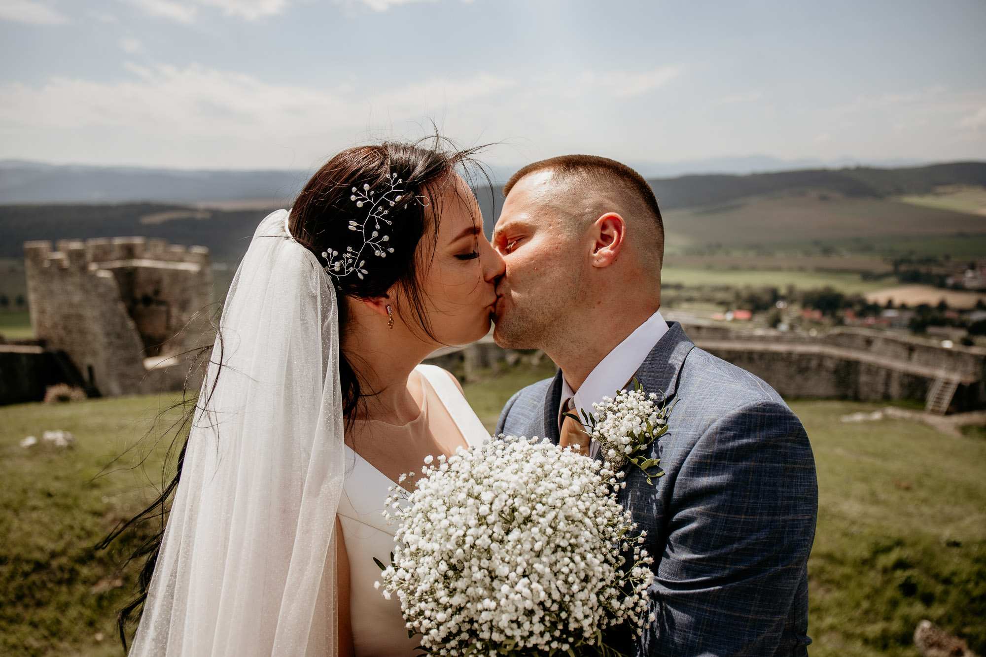 Dominika a Marián si vymieňajú romantický pohľad počas svadobného fotenia na Spišskom hrade, obklopení hradbami a zelenou prírodou.